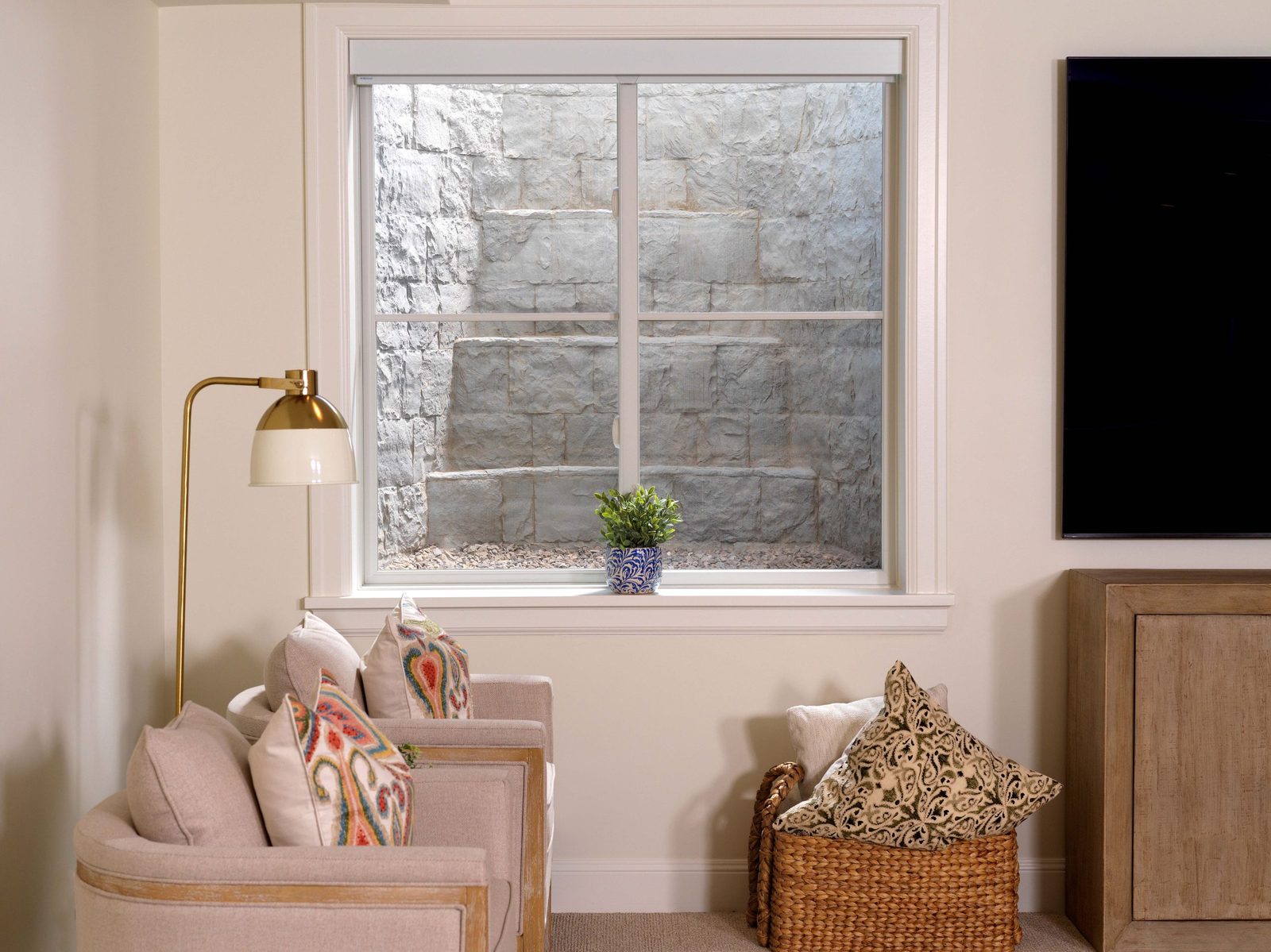 Bright finished basement sitting area with an egress window showing a stone-look well and its built-in steps